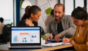 Team collaborating on digital marketing strategies with laptop displaying analytics and charts in a modern office setting.